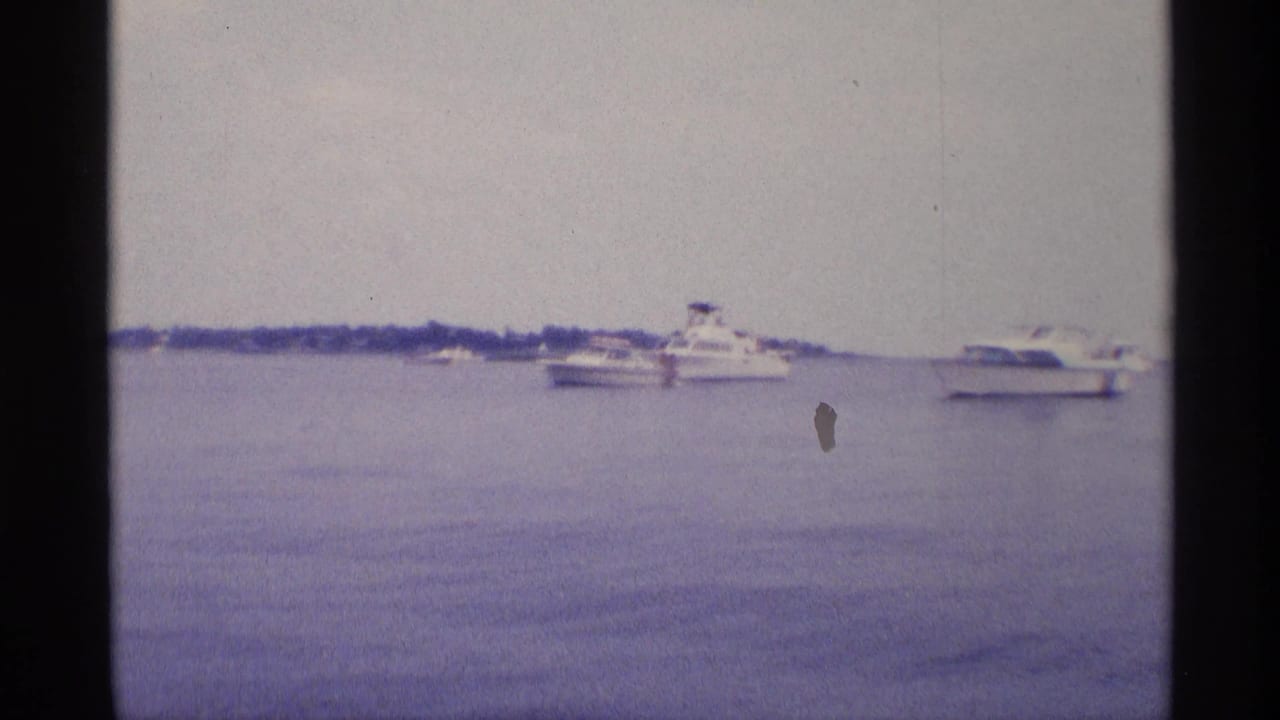 1973 New York lake scene with small motorboats and a larger white cruiser spread across calm water.