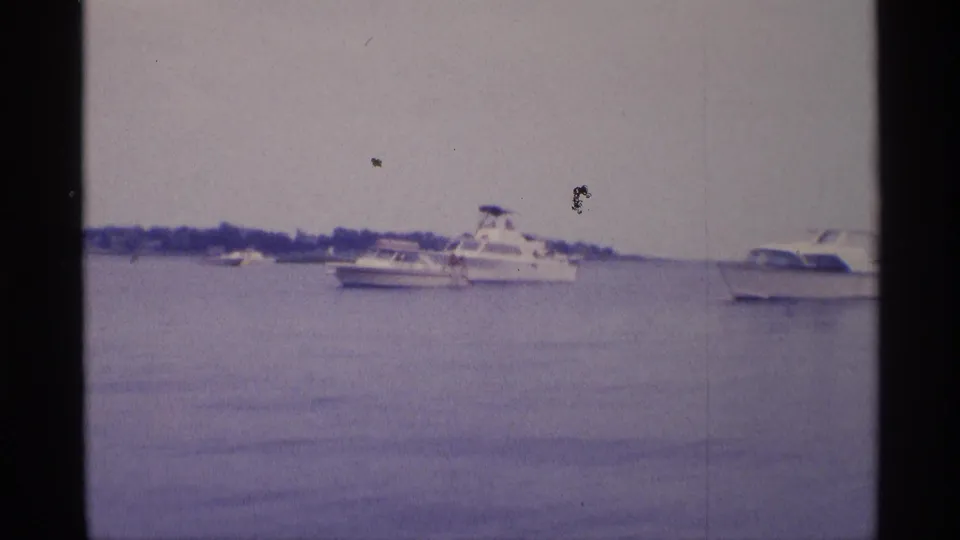 1973 New York 8mm frame showing a white cabin cruiser, smaller boats, and calm lake water.