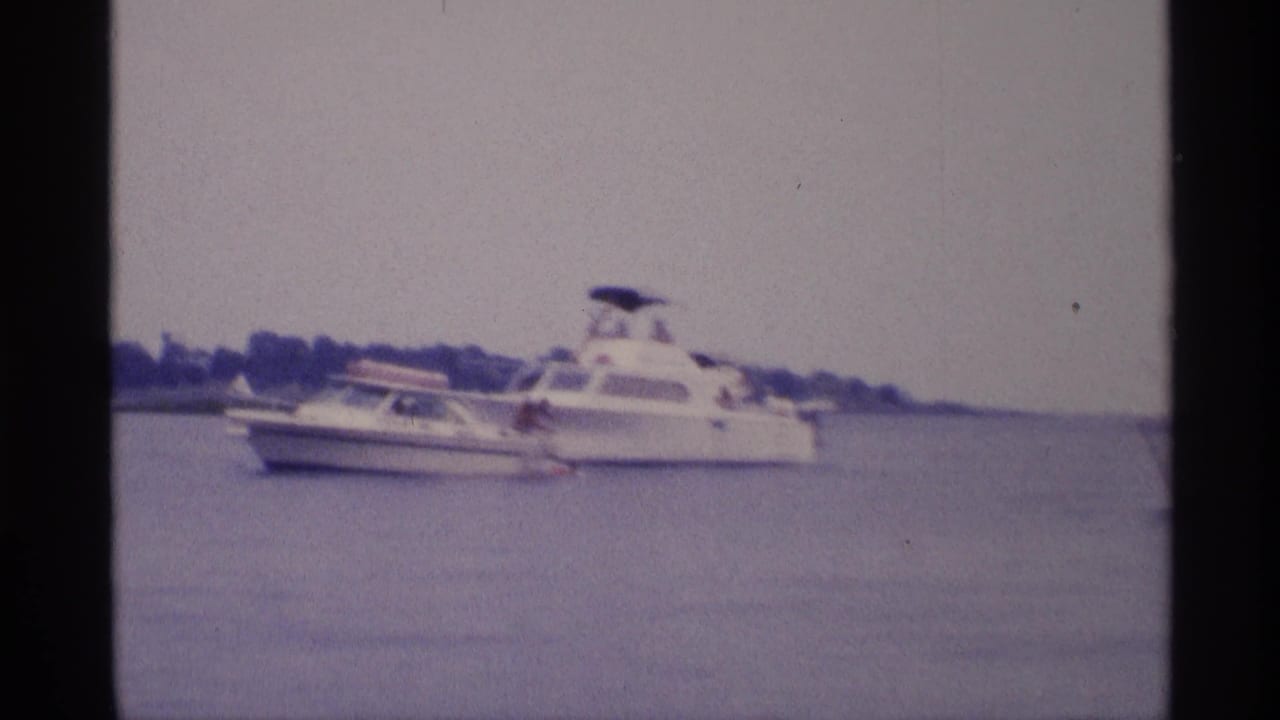 1973 New York lake footage frame with a small motorboat passing near a larger white cabin cruiser.