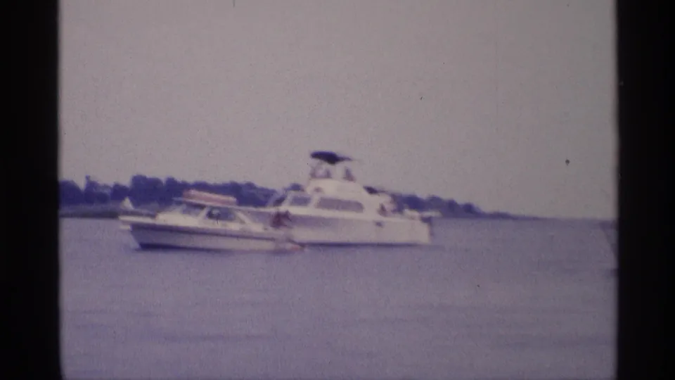 1973 New York lake footage frame with a small motorboat passing near a larger white cabin cruiser.