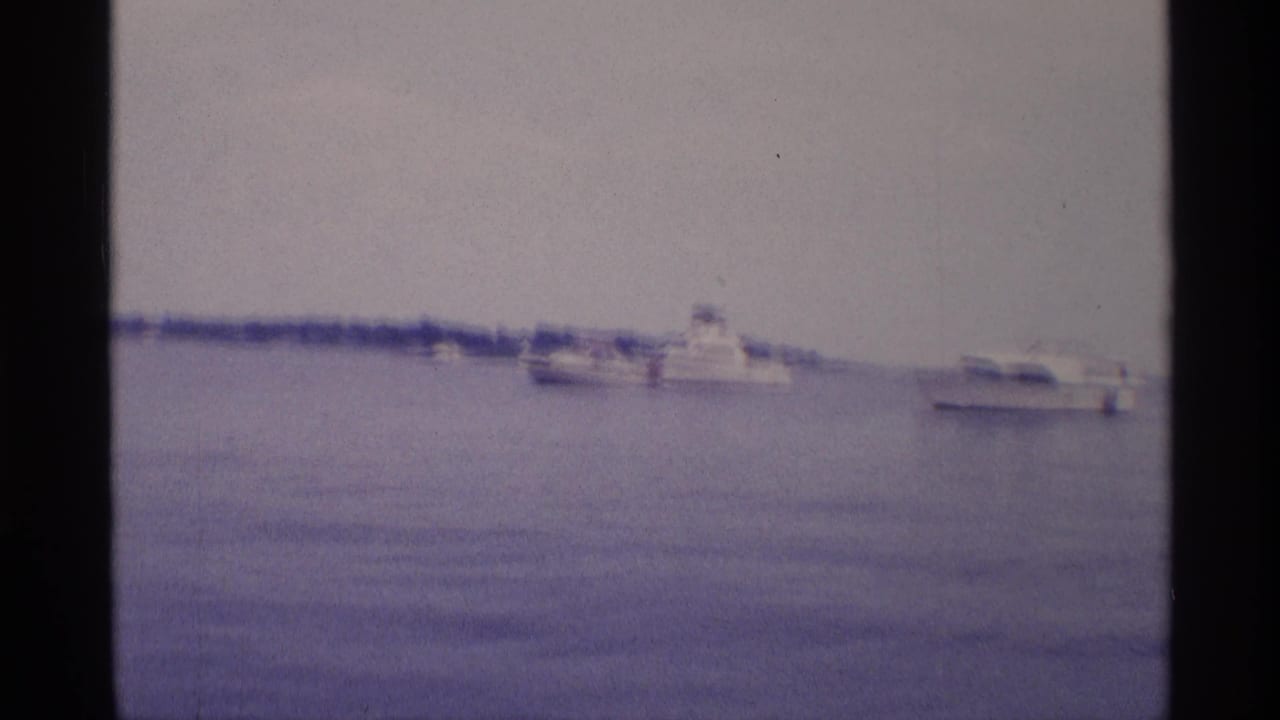 Distant white motorboats float across calm New York basin water in this soft 1973 8mm home-movie frame.