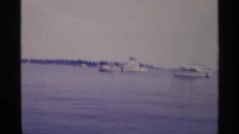 Distant white motorboats float across calm New York basin water in this soft 1973 8mm home-movie frame.
