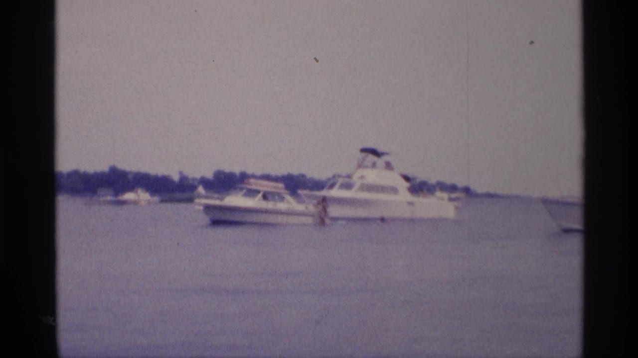 1973 New York 8mm frame with white pleasure boats on calm water and a small distant figure near a cabin cruiser.