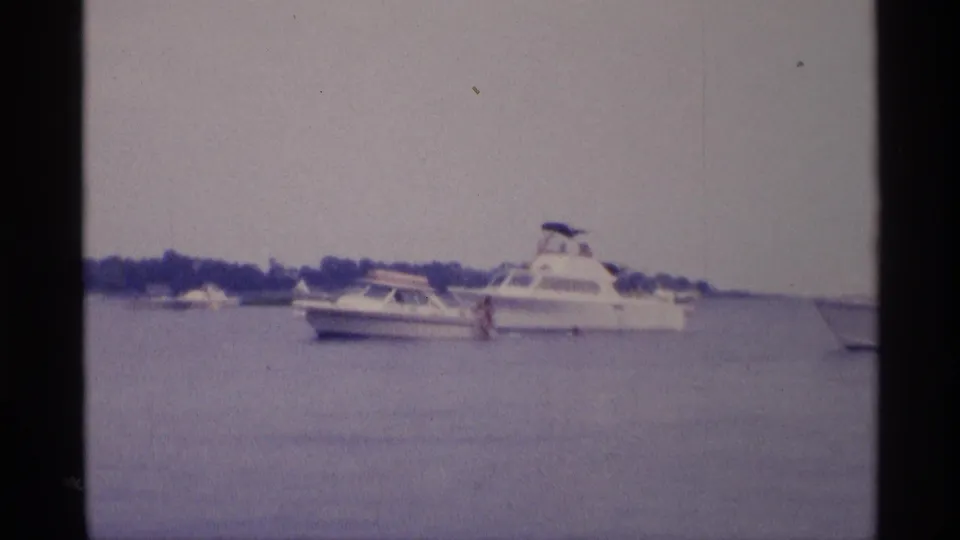 1973 New York 8mm frame with white pleasure boats on calm water and a small distant figure near a cabin cruiser.