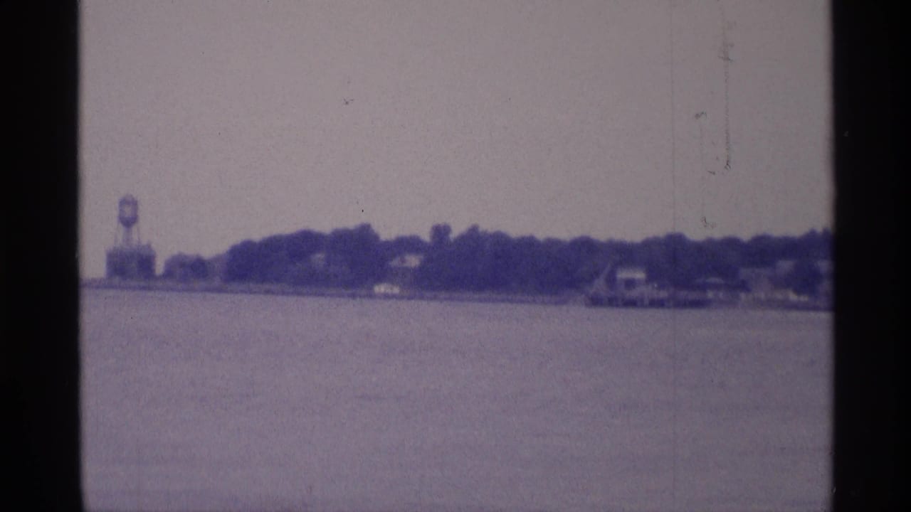Distant shoreline across water with a water tower at the left and dark film borders.