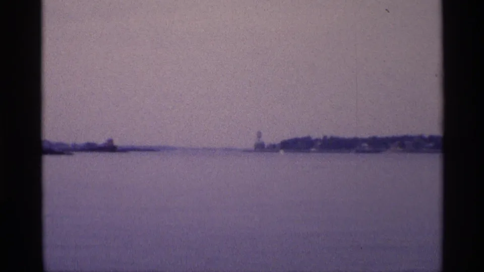1973 New York 8mm frame showing calm open water, hazy sky, and distant shoreline with a small structure near the horizon.