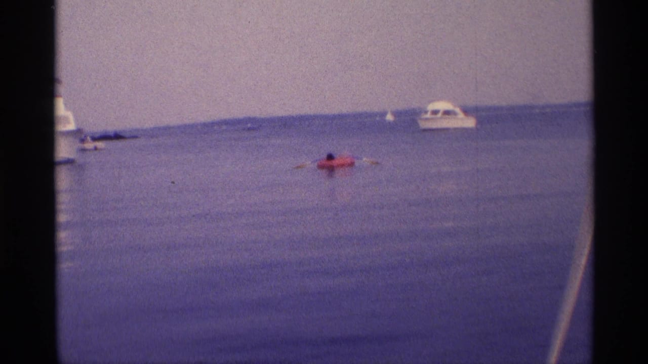 Person in a red inflatable raft paddling near a white motorboat on calm water.