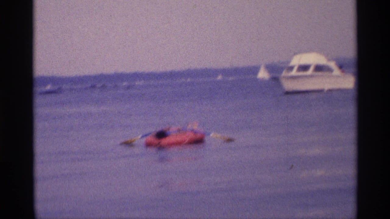 Woman on a red inflatable raft in calm water with a white motorboat in the background.