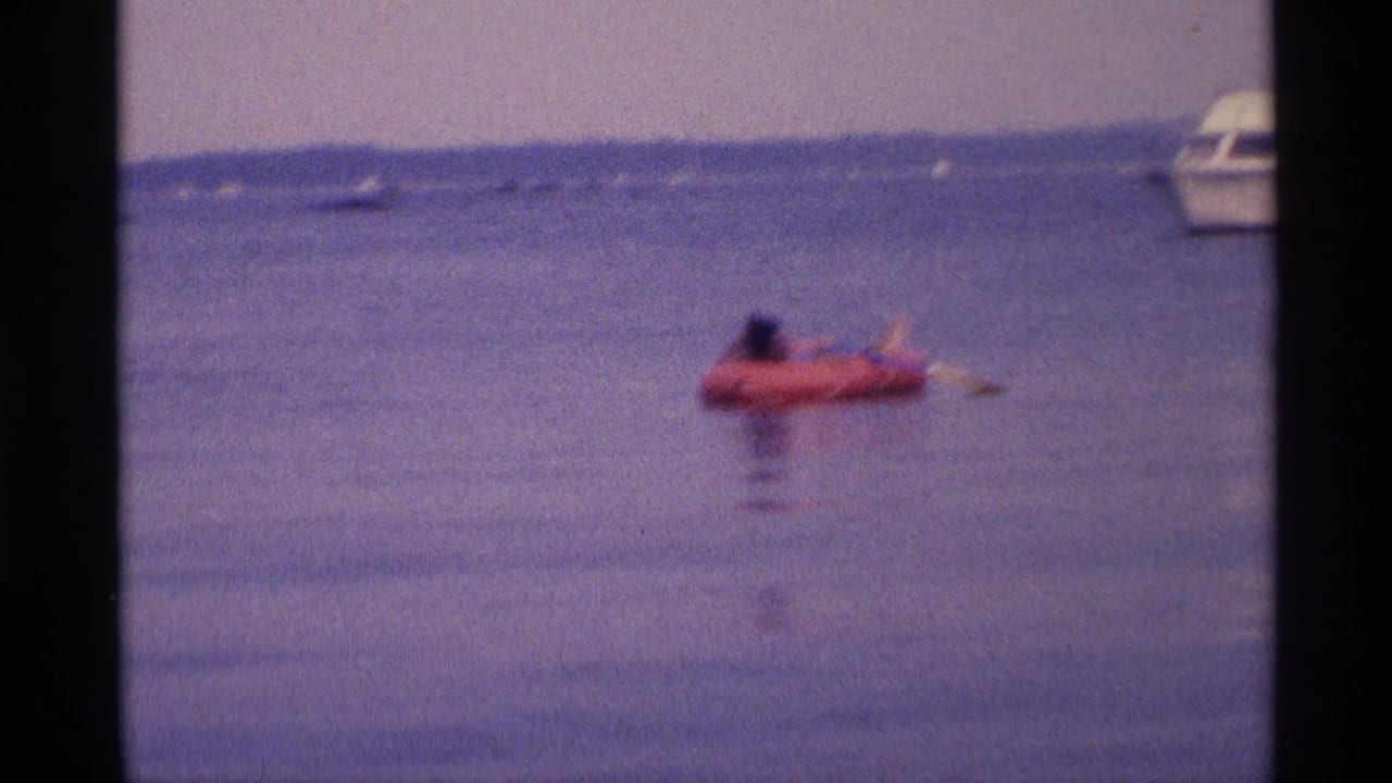 1973 New York 8mm frame showing the woman on a red raft near frame right, with a cropped white boat in the background.