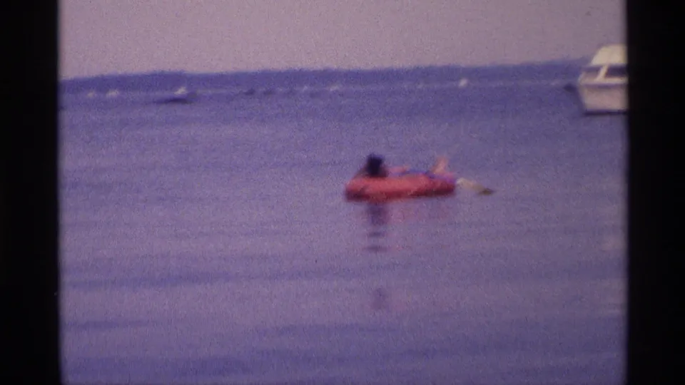 1973 New York 8mm frame showing the woman on a red raft near frame right, with a cropped white boat in the background.