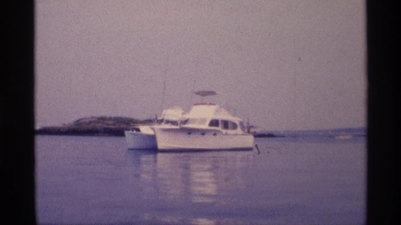White motorboat anchored on calm water with a low shoreline behind it.