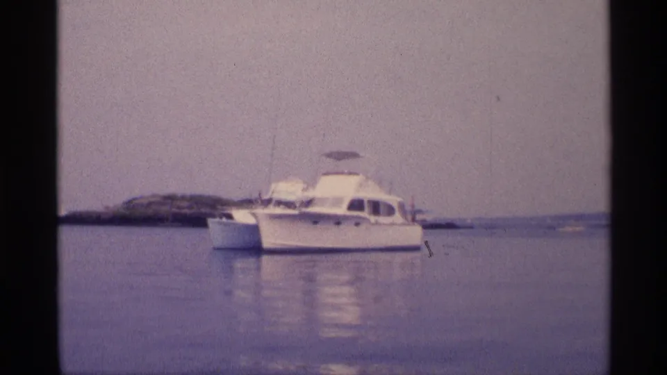 1973 New York 8mm frame showing a white motorboat on still water with a low shoreline in the background.