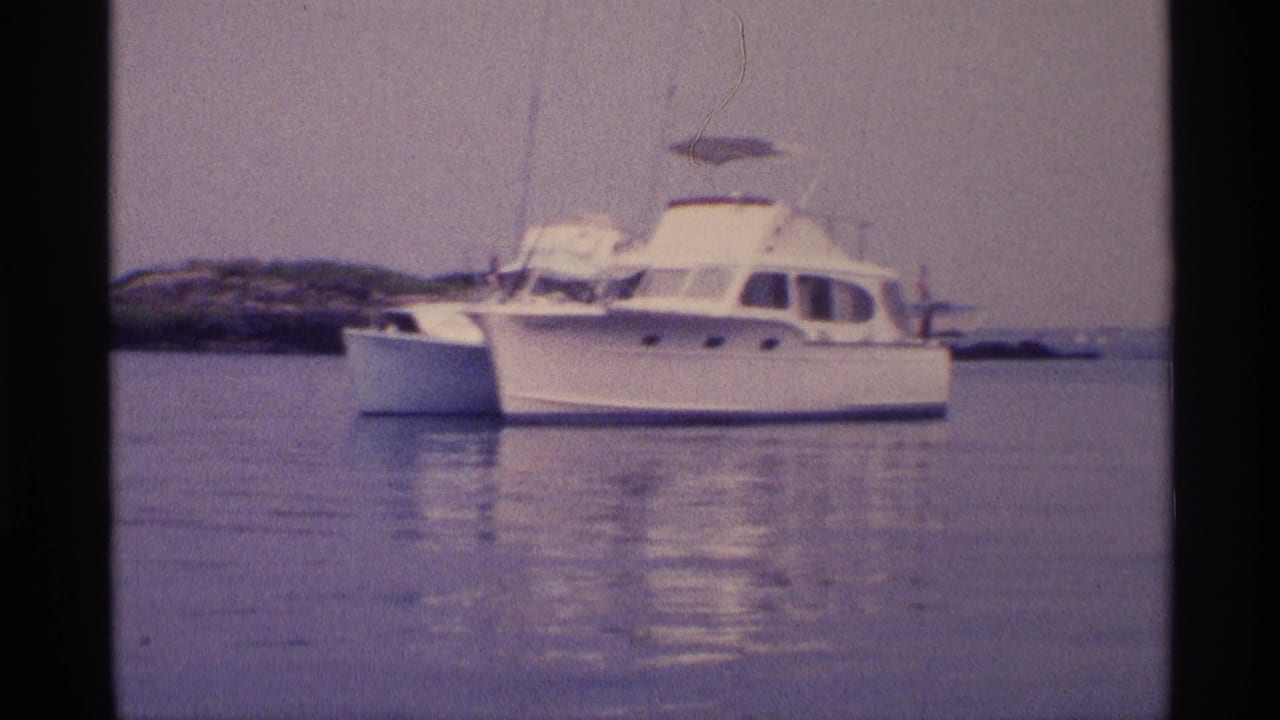 1973 New York home-movie frame with a white cabin motorboat, canopy and reflection on calm water.