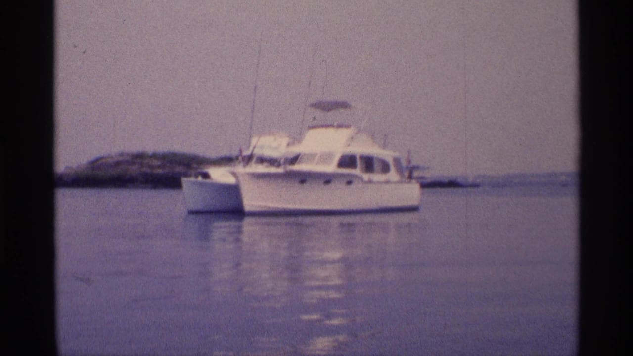 Soft 8mm frame of a white motorboat in calm New York-area water, with a low shoreline behind it.