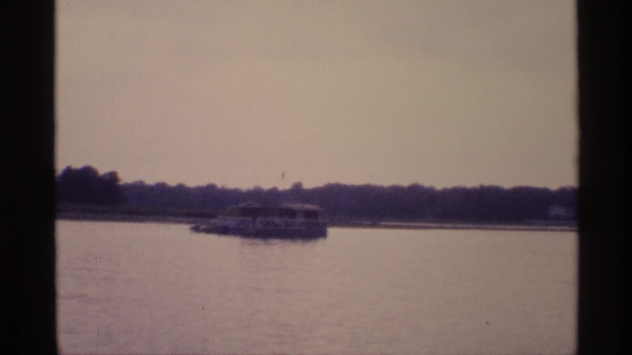 Small passenger boat crossing lake near a tree-lined shore.