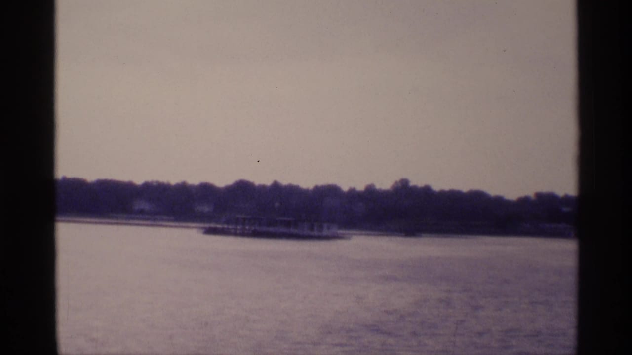 Distant wooded shoreline and low structures across calm water, framed by dark vertical boat edges.