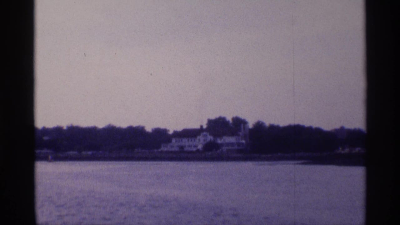 Distant white house across a broad river with trees along the shore.