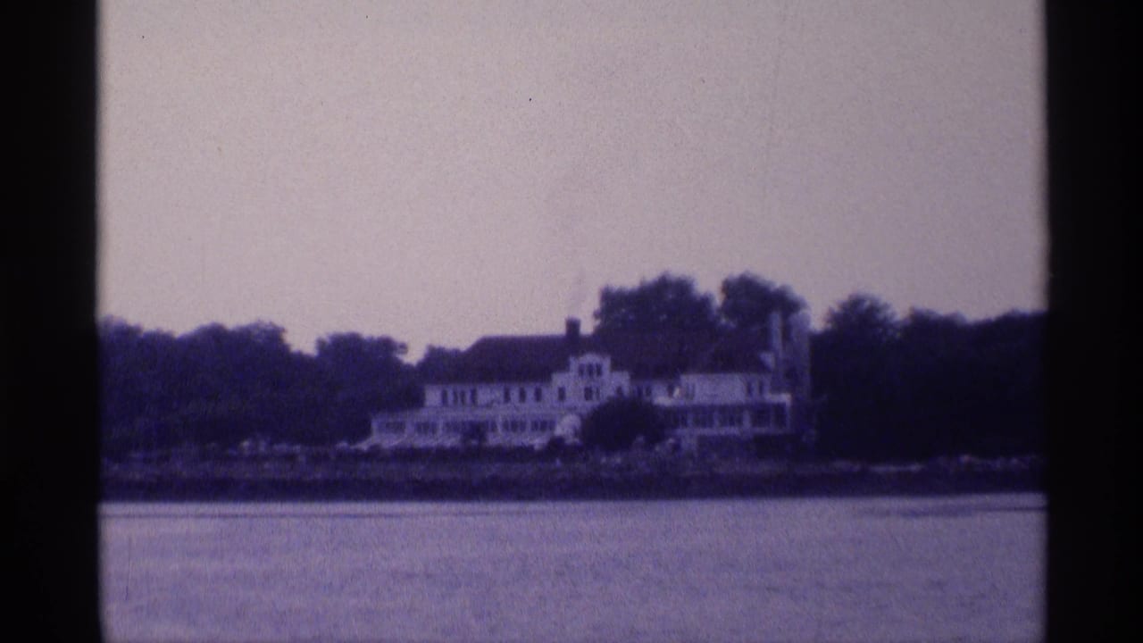 Large white waterfront house seen across the river, partly framed by trees.