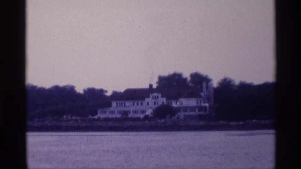 Large white house on a New York shoreline appears across the river, with trees, rooflines, and a soft purple-blue film cast.