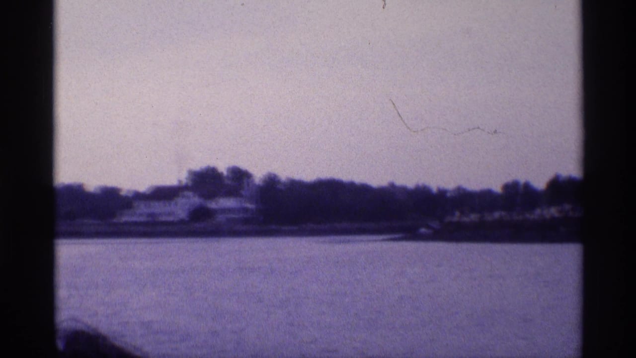 Wide 8mm frame from 1973 New York showing the white waterfront house farther away, with trees and calm water dominating the scene.