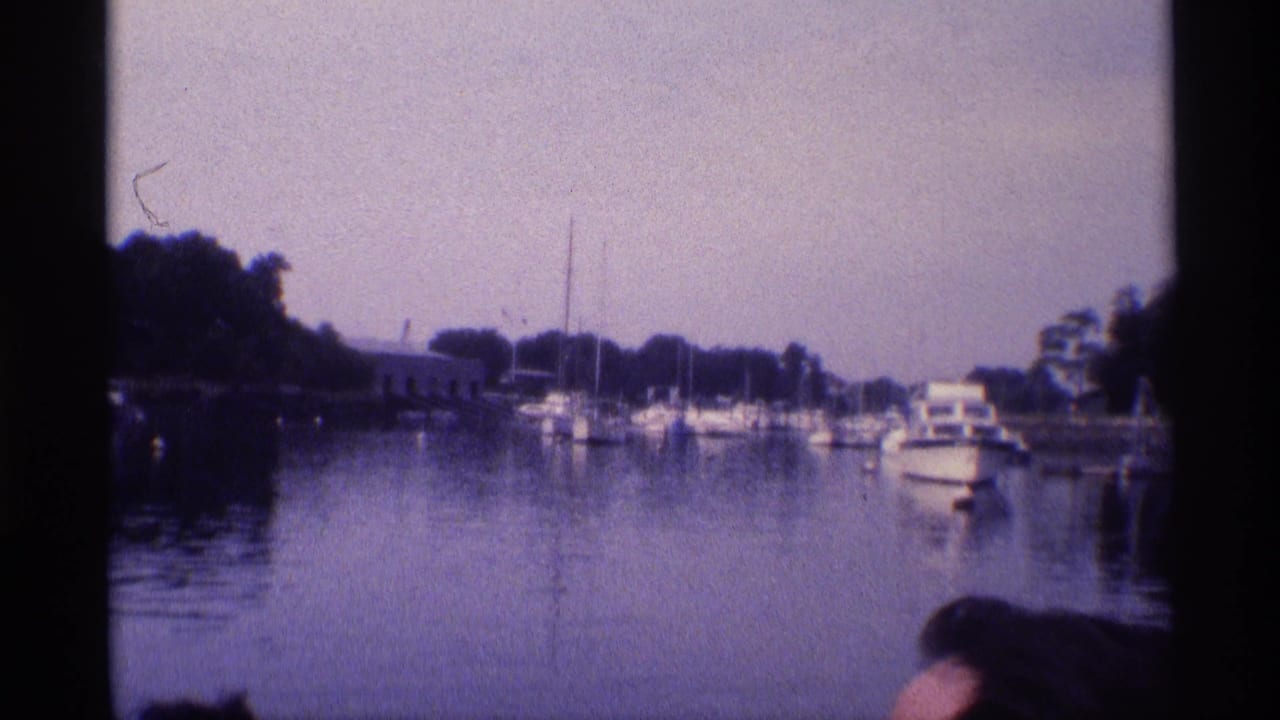 Boats moored across calm water with dark film borders and a partial onlooker at the bottom edge.