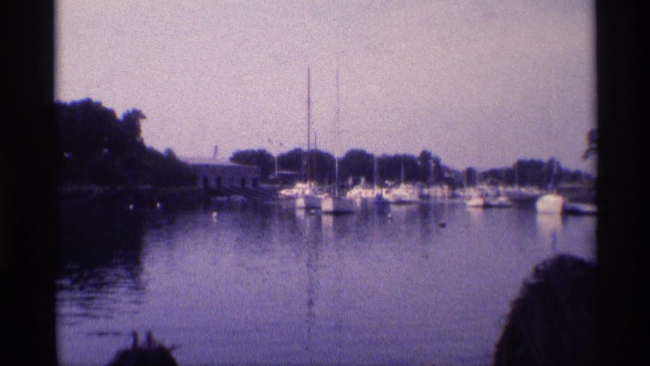 1973 New York 8mm view across a canal or marina, with moored boats and partial onlookers visible along the bottom edge.