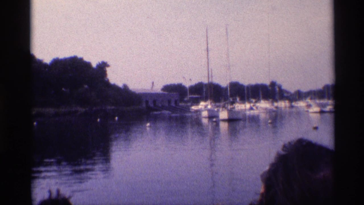 1973 New York marina footage showing white sailboats, tall masts, calm reflective water, and a partial foreground head.