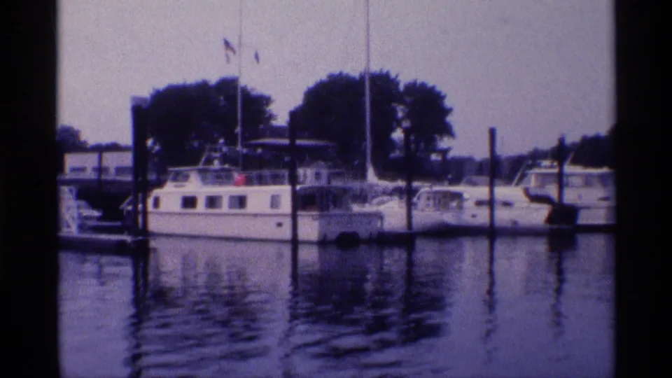 1973 New York marina view with white motor yachts and sailboats tied near dark pilings under a hazy sky.