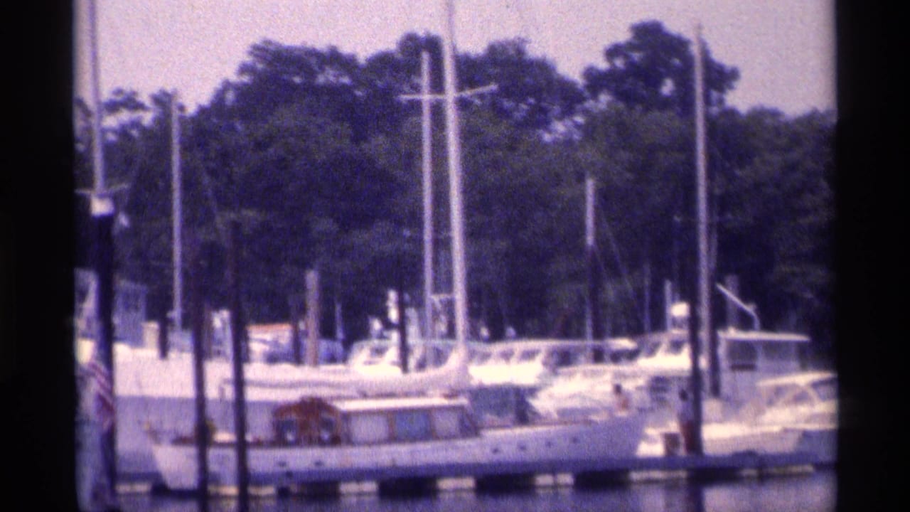 Sailboats and motor yachts docked beside pilings on calm water.