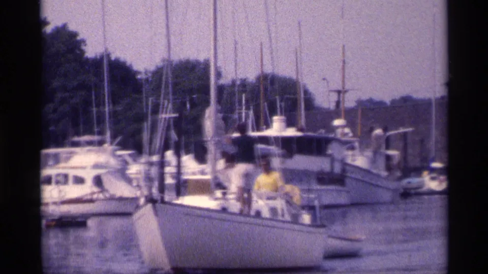 Soft 8mm frame from 1973 New York showing a marina, clustered masts, docked boats, and people on a white sailboat.
