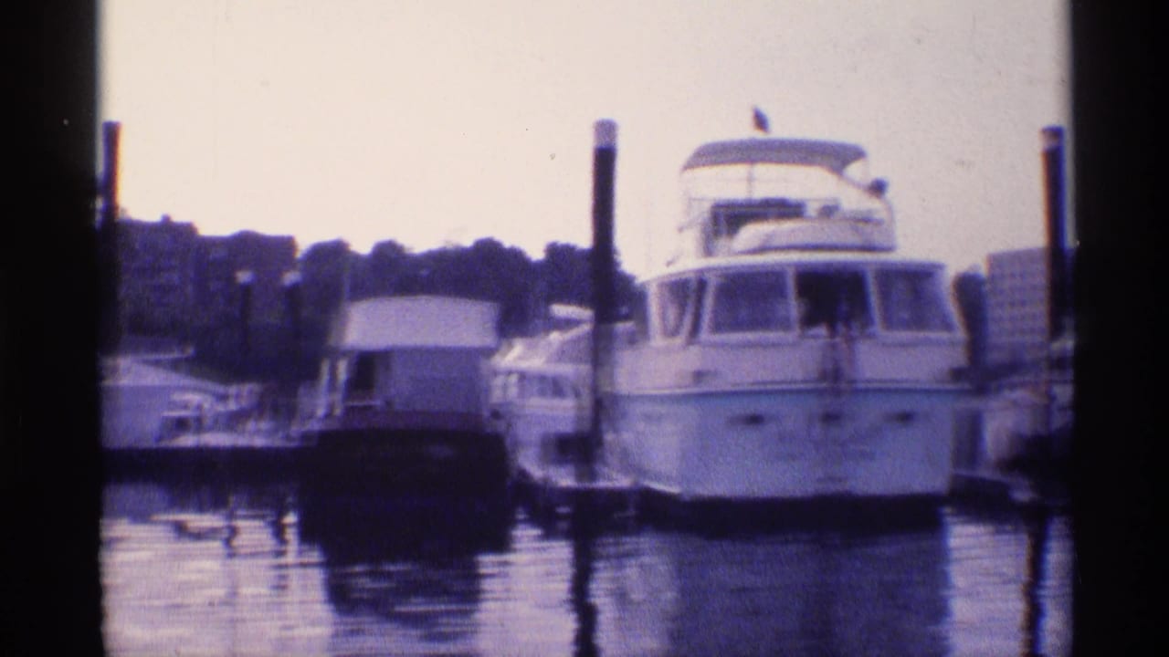 A large white motor yacht is moored among smaller boats at a New York marina, with still water and wooden dock posts visible.
