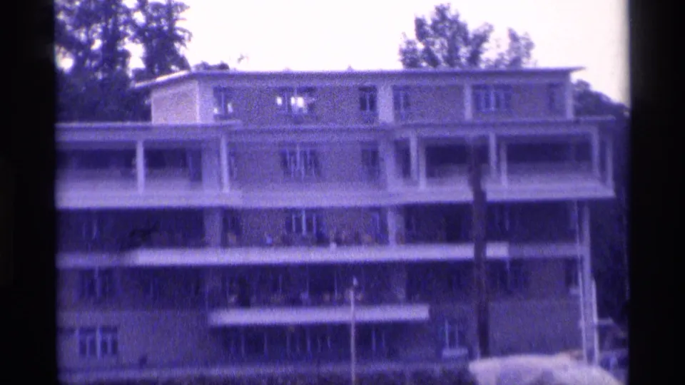 1973 New York 8mm frame showing a waterfront apartment building with balconies, windows, and trees behind it.