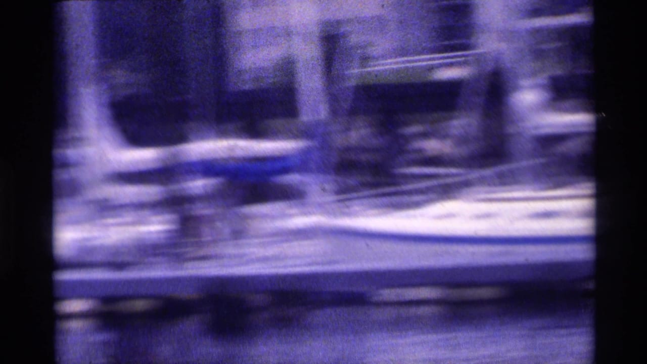 Motion-blurred 1973 New York waterfront view with dock structures and boats seen from a moving boat.