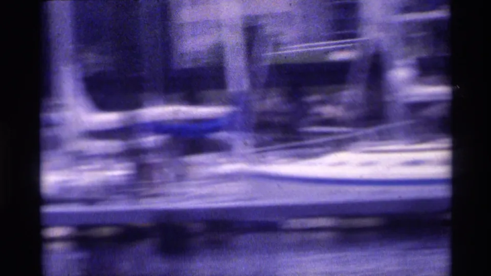 Motion-blurred 1973 New York waterfront view with dock structures and boats seen from a moving boat.
