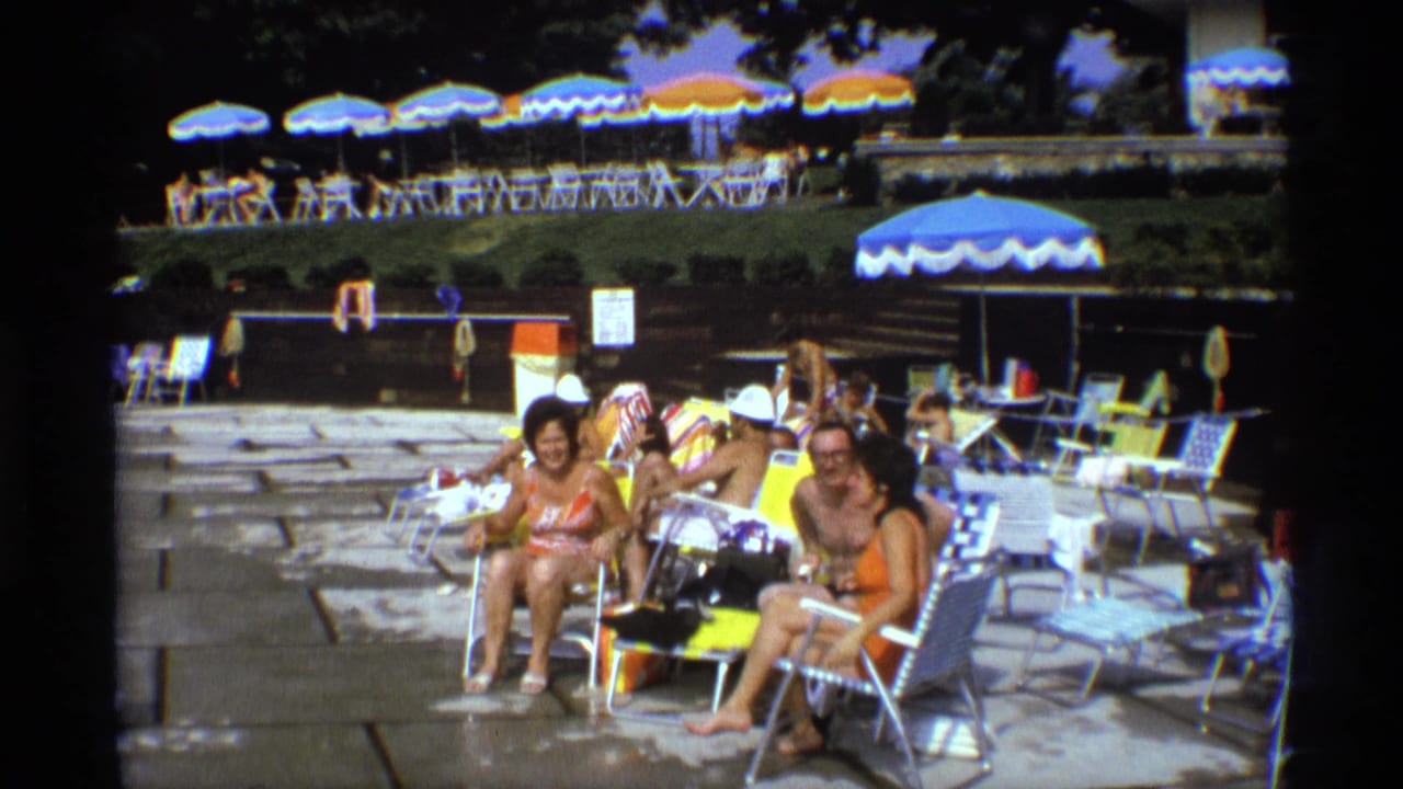 Adults at a New York pool in 1973 sit and smile toward the camera amid lounge chairs and umbrellas.