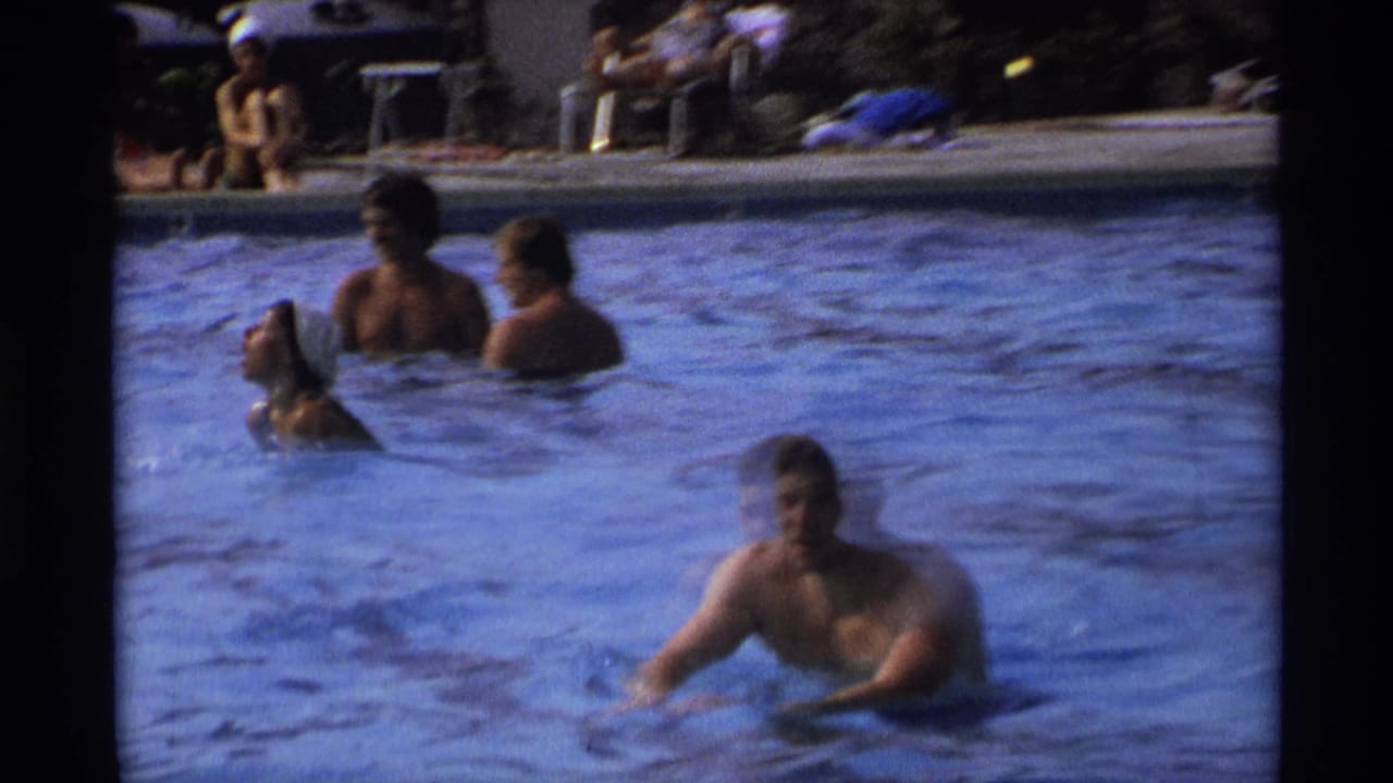 Swimmers in a crowded outdoor pool with lounge chairs along the deck.