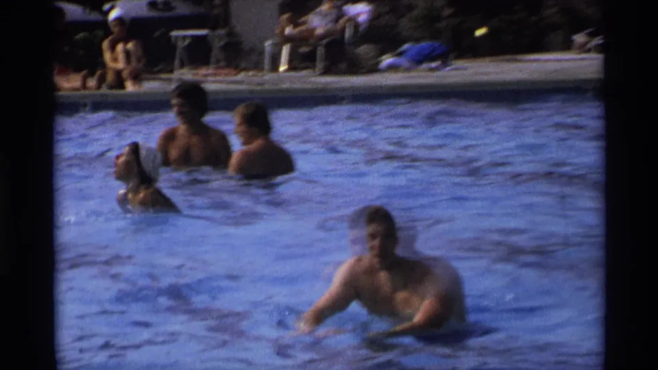 1973 New York home-movie frame showing several people in an outdoor public pool as one man begins moving through the water.