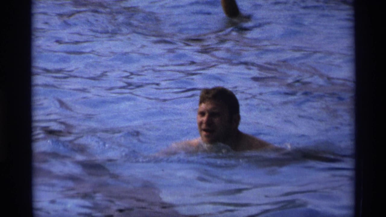 1973 New York 8mm frame showing a man partly submerged and swimming in a public pool, with soft focus and visible film grain.