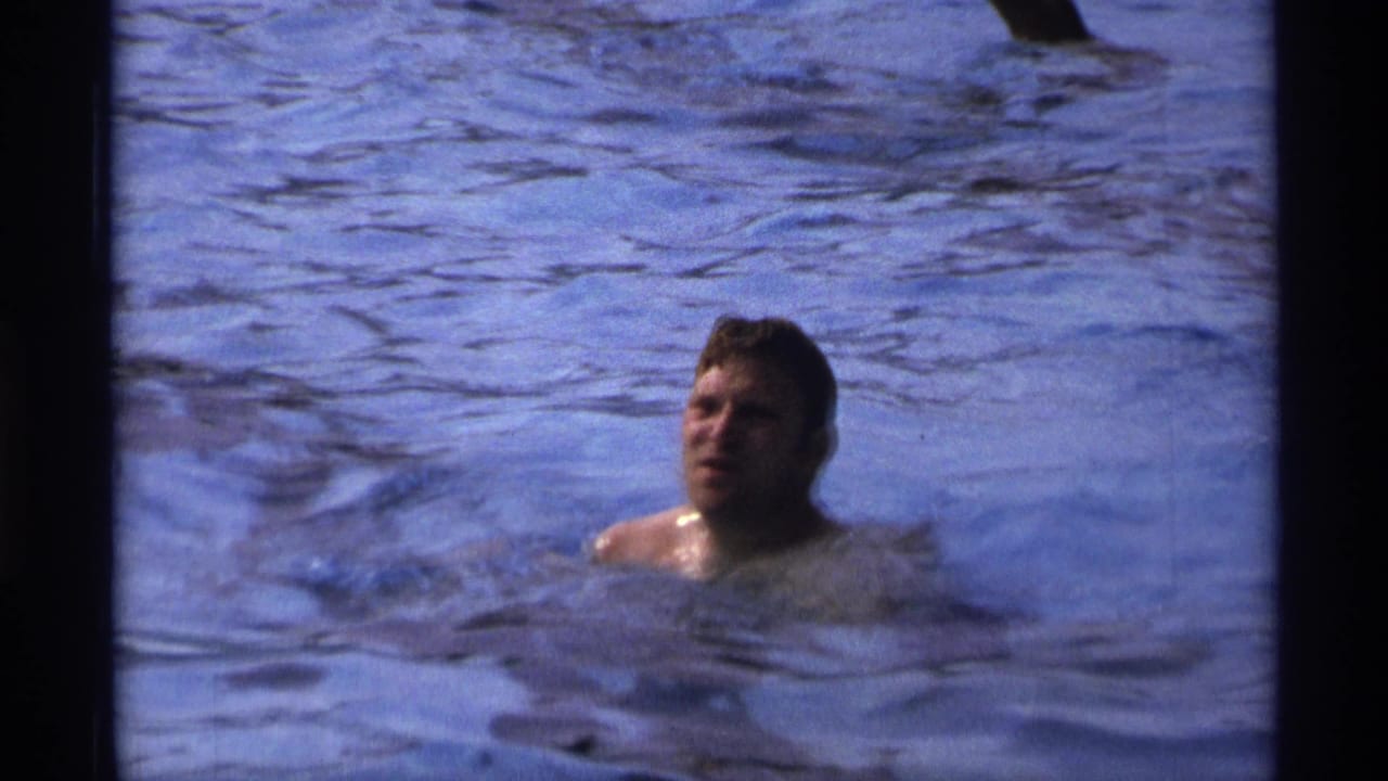 1973 New York home-movie still of a man in a public swimming pool, framed closely amid blue water and visible film grain.