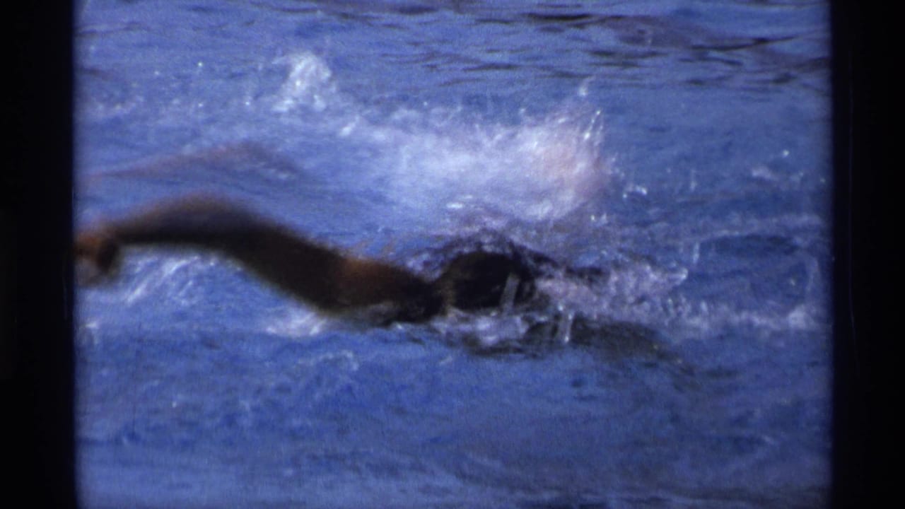 Swimmer doing freestyle in blue pool water with splashes around the arms.