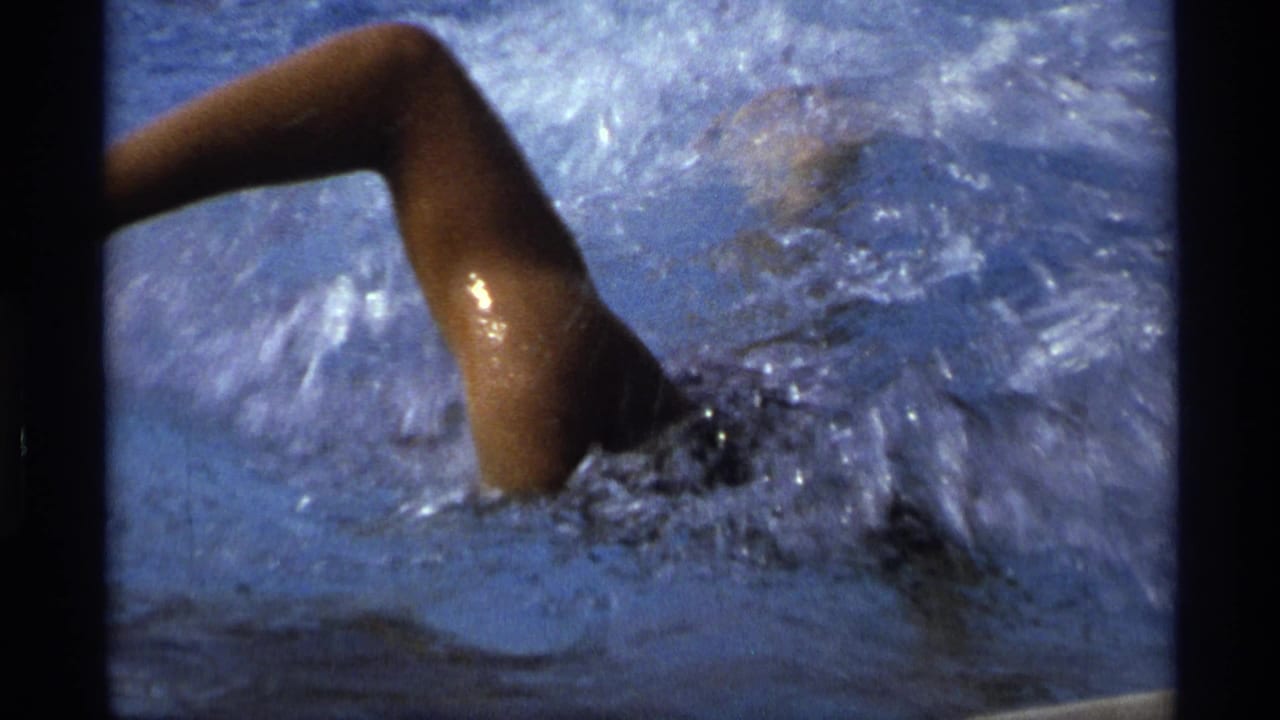 Close 8mm view of a swimmer in a dark swimsuit cutting through pool water in 1973 New York footage.