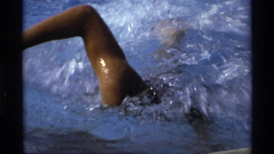 Close 8mm view of a swimmer in a dark swimsuit cutting through pool water in 1973 New York footage.