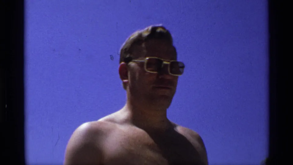 In the closing frame, the shirtless man in gold-rimmed sunglasses turns slightly sideways against the bright blue sky.