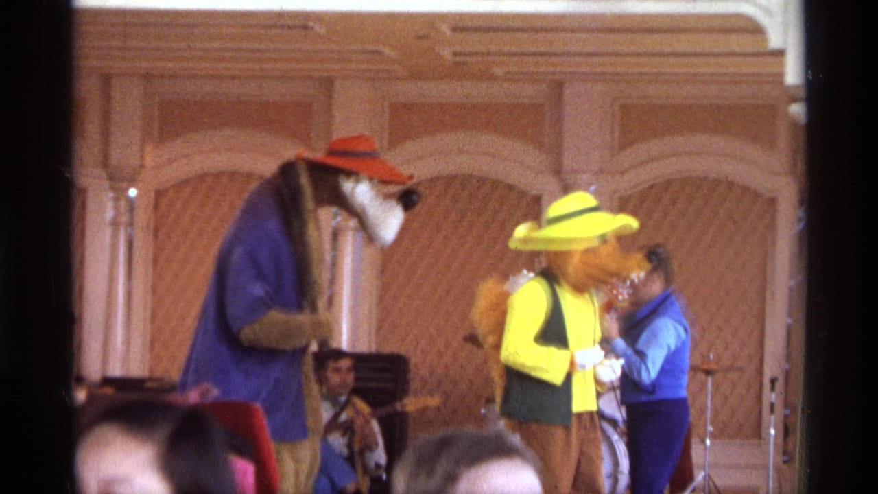1974 Orlando 8mm frame showing two costumed stage characters performing before a live band, viewed from the audience.