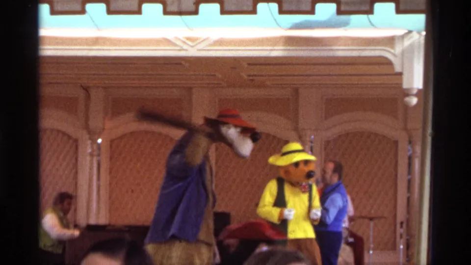 Warm 1974 Orlando 8mm frame of costumed characters in a stage skit, with a prop bat, band, and audience heads visible.