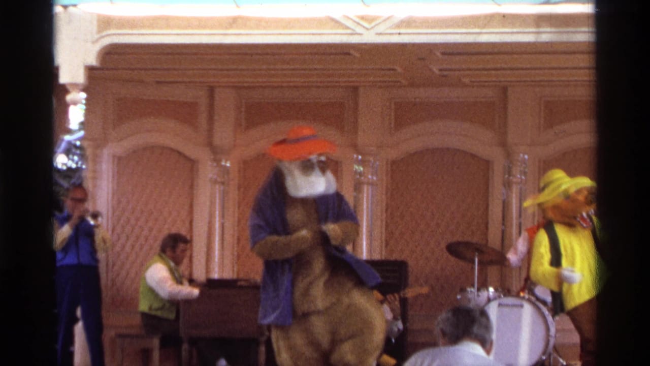Costumed bear mascot dances on stage while musicians perform nearby.