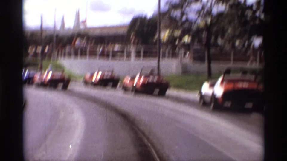 Motion-blurred 1974 Orlando home-movie frame of several go-karts traveling along a park track past grass, trees, and railings.