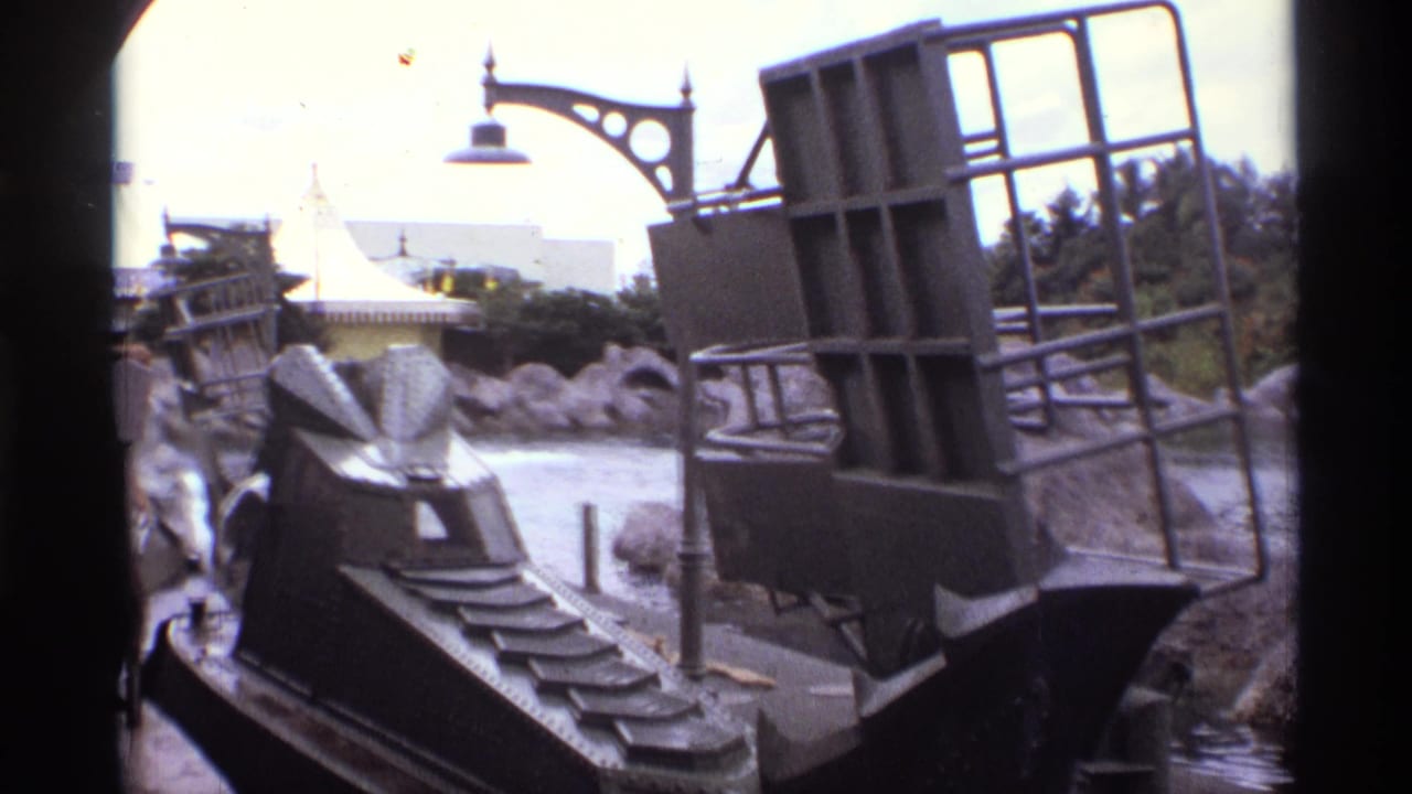 1974 Orlando home-movie frame showing a dark ride vehicle passing artificial rocks and a decorative lamp along a waterway.