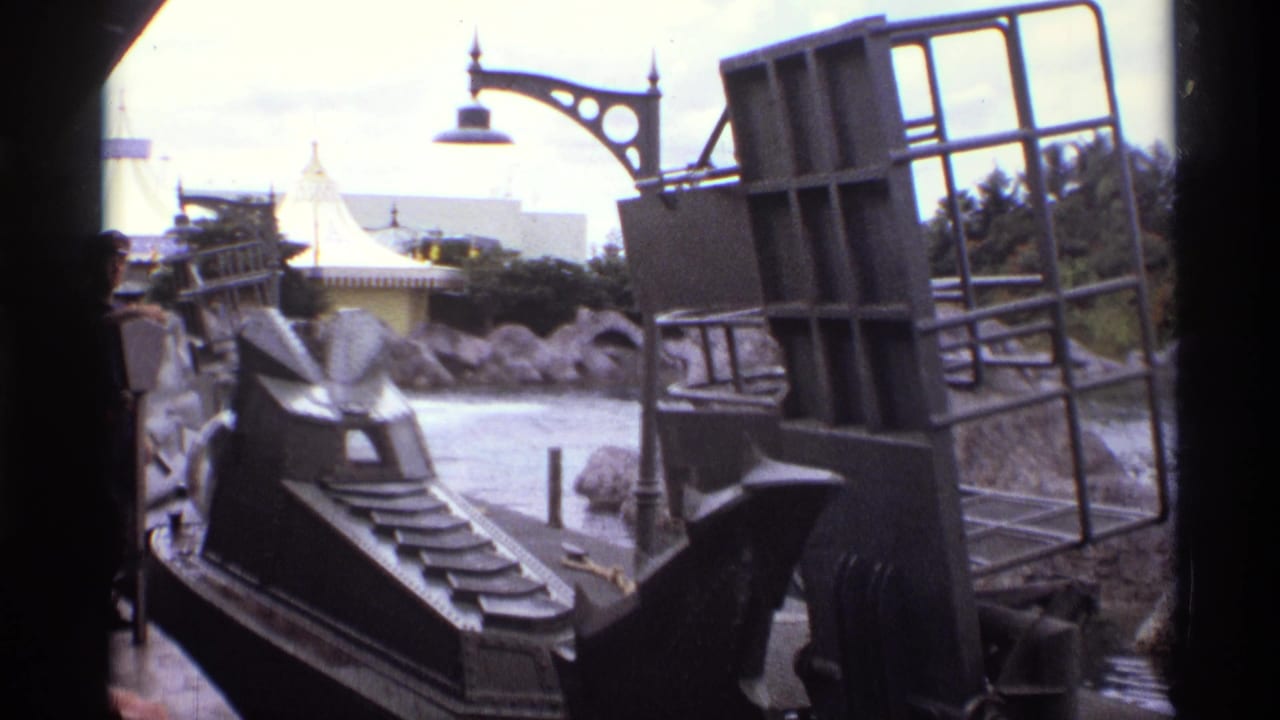 1974 Orlando 8mm frame with a dark ride vehicle structure, steps, railing, artificial rocks, and themed lamp visible from a boat.