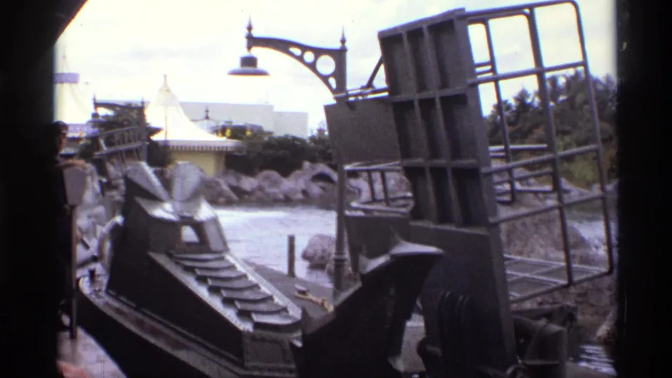 1974 Orlando 8mm frame with a dark ride vehicle structure, steps, railing, artificial rocks, and themed lamp visible from a boat.